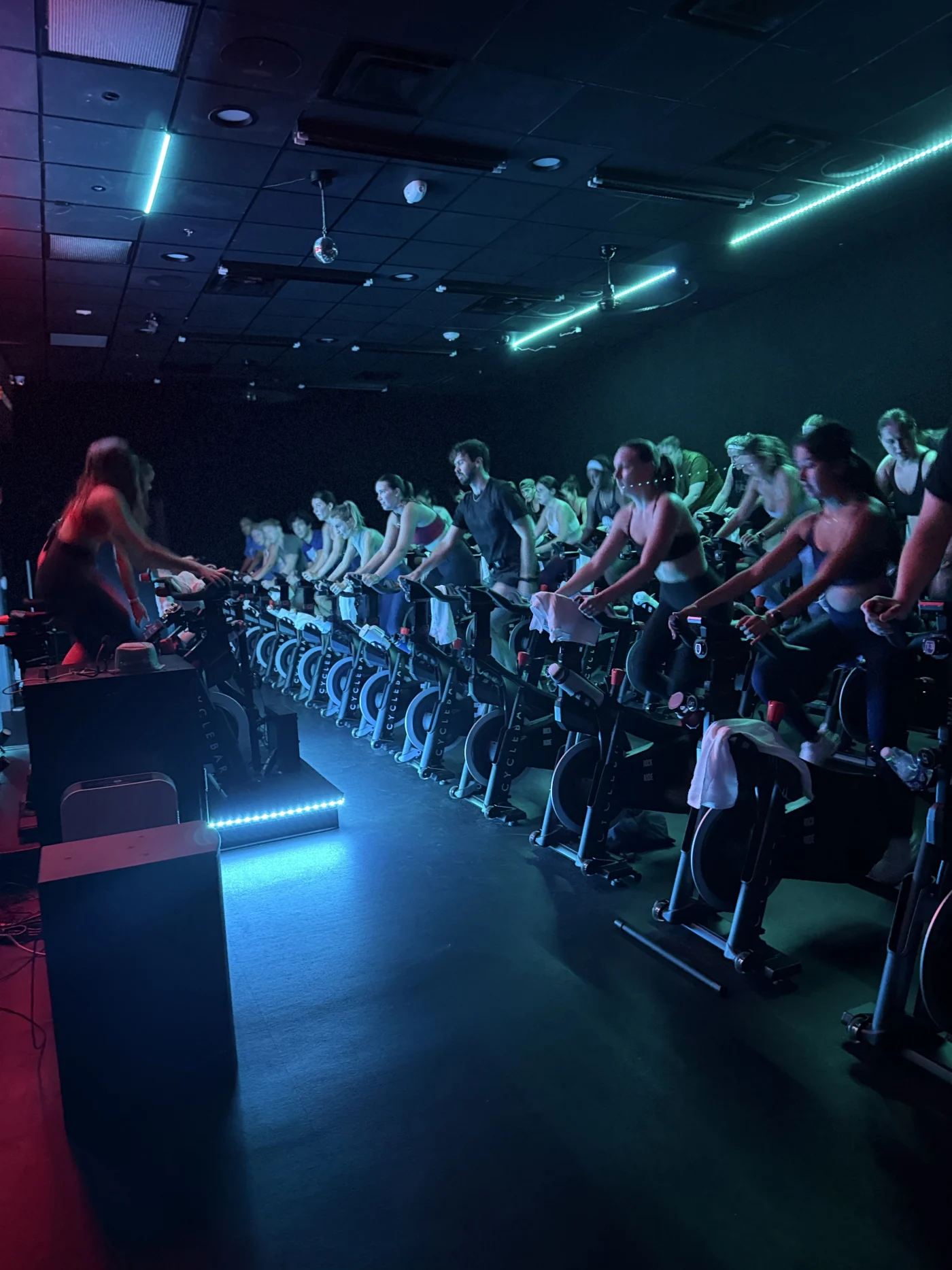 A full class riding in the CycleTheatre under teal stage lights